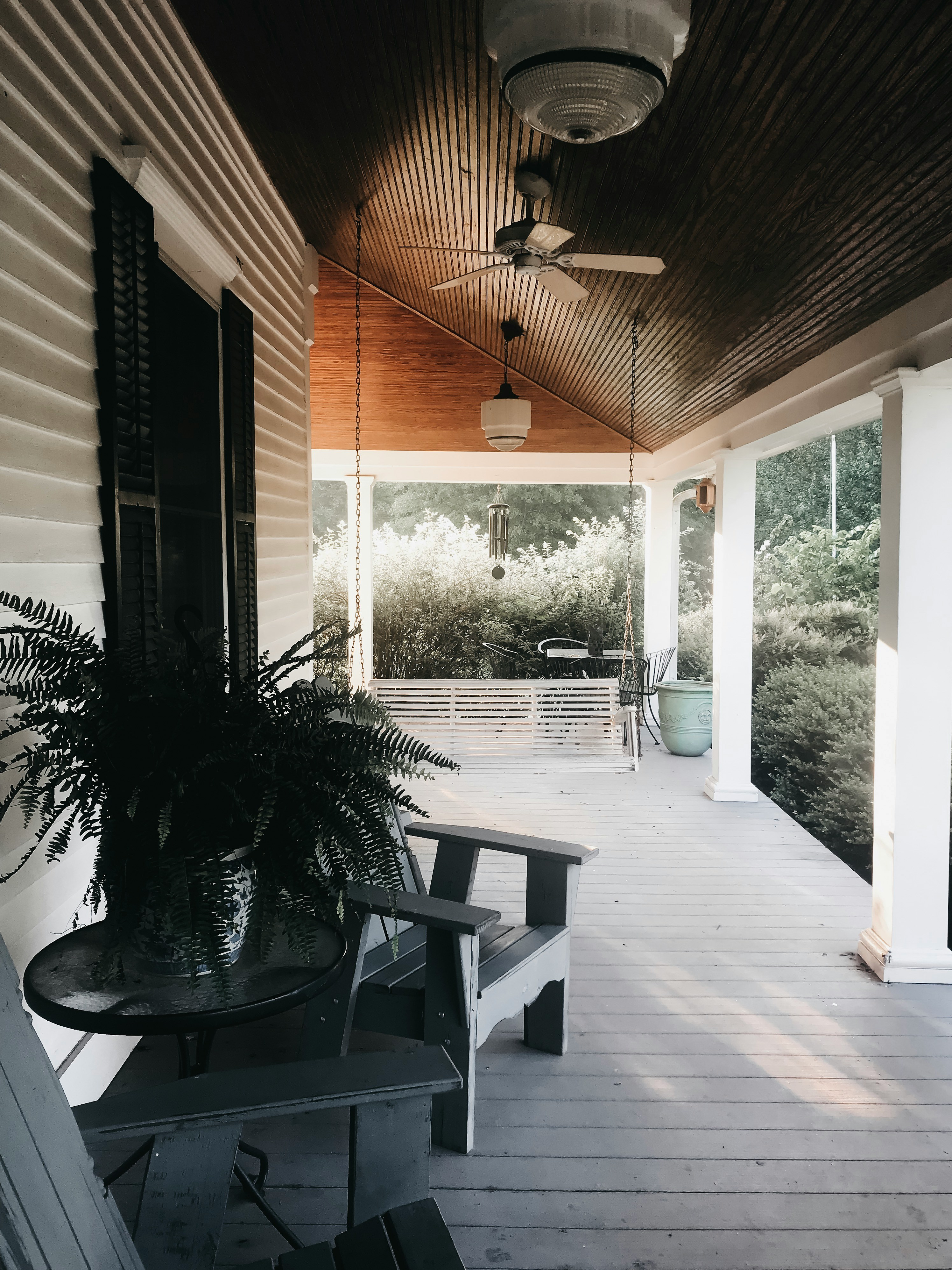 Warm front porch with wooden ceiling, ceiling fan, Adirondack chair and fern